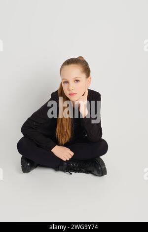 Das junge Mädchen sitzt im Kreuz auf dem Boden, schaut auf und hört jemandem aufmerksam zu Stockfoto