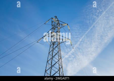 Unteransicht eines Hochspannungsturms mit blauem Himmel im Hintergrund mit Chemtrails Stockfoto