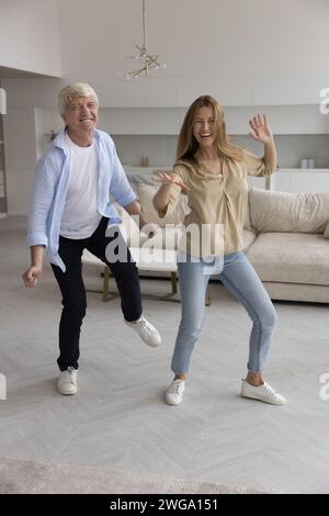 Fröhliche Tochter und fröhlicher, energiegeladener älterer Vater tanzen zusammen Stockfoto