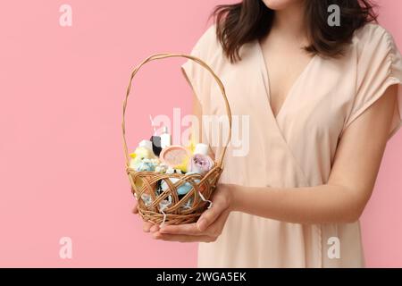 Frau, die einen Osterkorb mit dekorativer Kosmetik auf rosa Hintergrund hält Stockfoto