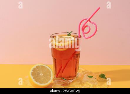 Eiszitronentee mit herzförmigem Strohhalm. Es Zitronentee auf rosa und gelbem Hintergrund Stockfoto