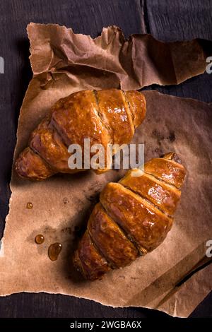 Im Vordergrund, mit Blick von oben, zwei appetitlich duftende Croissants auf Backpapier. Stockfoto