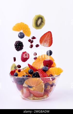 Das in Stücke gemischte frische Obst fällt in die Glasschale. Weißer Hintergrund Stockfoto