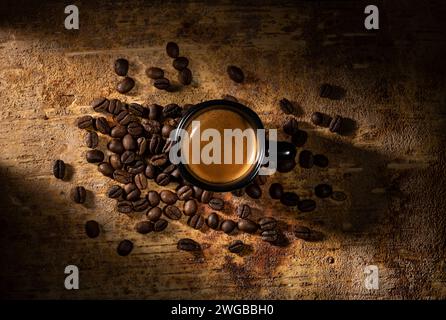 Im Vordergrund, von oben, auf dem strukturierten braunen rustikalen Hintergrund, eine Tasse italienischen Espresso und einige geröstete Kaffeebohnen. Stockfoto