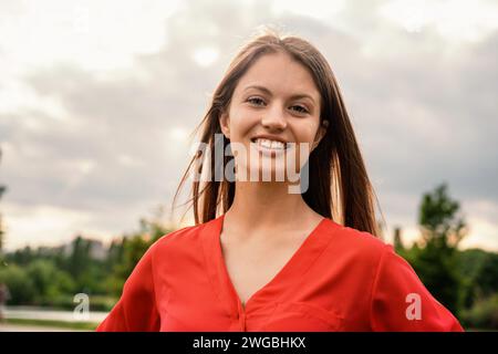 Eine junge Frau in einer roten Bluse lächelt hell und strahlt Vertrauen in eine ruhige Umgebung aus. Stockfoto