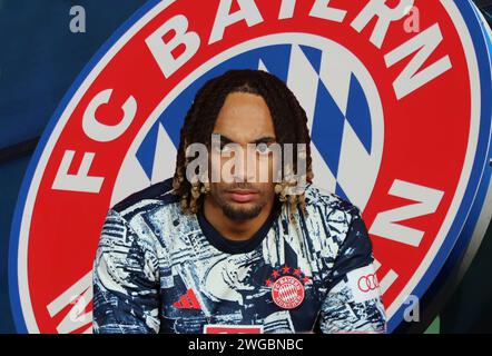 München, Deutschland 04. Februar 2024: Fussball, Herren, Bundesliga, Saison 2023/2024, FC Bayern München ! Achtung Fotomontage! Hier im Bild Sacha Boey (FC Bayern München) Kopf, Oberkörper, im Hintergrund das Logo des Vereins Stockfoto