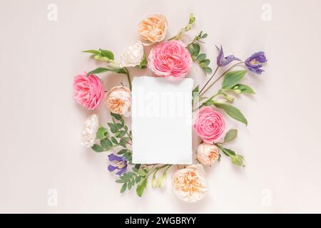 Blick von oben auf Rosen, Chrysanthemen und Alstroemeria-Blumen, die um eine leere weiße Karte angeordnet sind Stockfoto