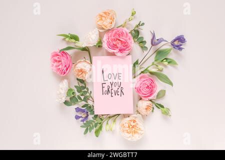 Blick von oben auf Rosen, Chrysanthemen und Alstroemeria-Blumen, die um eine Valentinskarte mit den Worten Love You Forever angeordnet sind Stockfoto