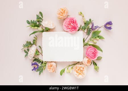 Blick von oben auf Rosen, Chrysanthemen und Alstroemeria-Blumen, die um eine leere weiße Karte angeordnet sind Stockfoto