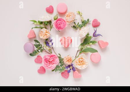 Blick von oben auf ein Blumenarrangement mit Rosen, Chrysanthemen, Alstroemeria-Blumen und Laub um herzförmige Süßigkeiten auf rosa Hintergrund Stockfoto