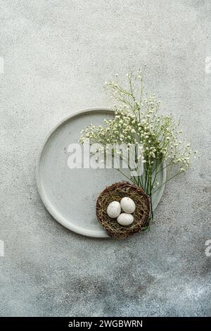 Blick von oben auf weiße gypsophila-Blumen und ein Vogelnest mit Ostereiern auf einer Keramikplatte Stockfoto