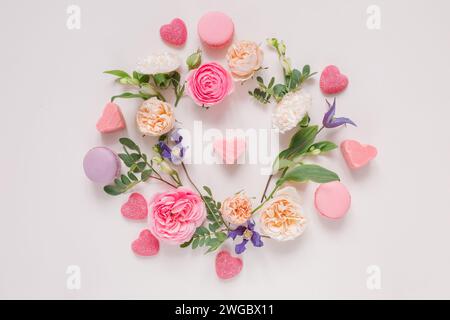 Blick von oben auf ein Blumenarrangement mit Rosen, Chrysanthemen, Alstroemeria-Blumen und Laub um herzförmige Süßigkeiten auf rosa Hintergrund Stockfoto