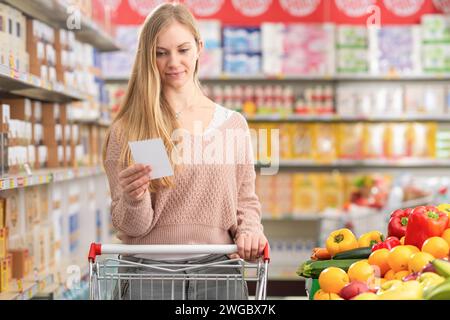 Attraktive junge Frau schiebt einen Einkaufswagen und kauft Lebensmittel im Supermarkt Stockfoto