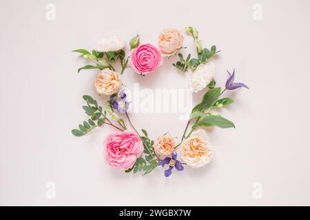 Blick von oben auf ein kreisförmiges Blumenarrangement aus Rosen, Chrysanthemen, Alstroemeria-Blumen und Laub auf rosa Hintergrund Stockfoto