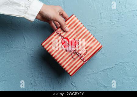 Die Hand einer Frau, die eine Geschenkbox hält, die mit Herzen verziert ist Stockfoto