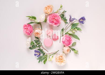 Blick von oben auf ein Blumenarrangement mit Rosen, Chrysanthemen, Alstroemeria-Blumen und Laub um herzförmige Süßigkeiten auf rosa Hintergrund Stockfoto