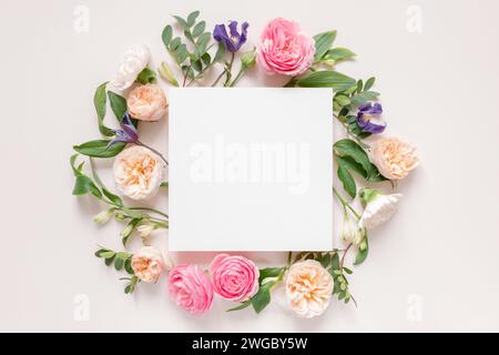 Blick von oben auf Rosen, Chrysanthemen und Alstroemeria-Blumen, die um eine leere weiße Karte angeordnet sind Stockfoto