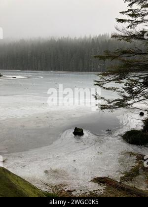 Ein ruhiger Teich umgeben von schneebedeckten Bäumen und majestätischen Felsen Stockfoto