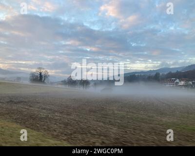 Ein Sonnenuntergang über einem nebeligen Feld mit Häusern und Gras Stockfoto