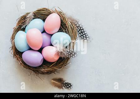 Happy Easter Konzept. Vorbereitung auf den Urlaub. Farbenfrohe, pastellfarbene Ostereier im Nest mit Federn auf betonsteingrauem Hintergrund. Einfacher Minimalismus flach Lay Draufsicht Kopieplatz Stockfoto