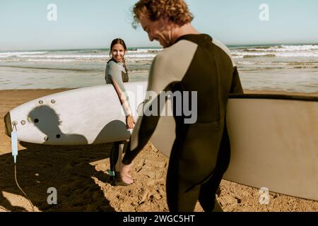 Ein paar Surfer im Wetsuit mit Surfbrettern stehen am Strand und lächeln Stockfoto