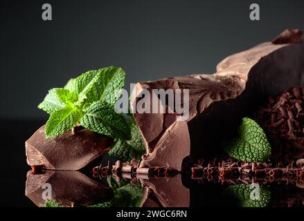 Stücke von dunkler Bitterschokolade und Schokoladenchips mit Minze auf schwarzem reflektierendem Hintergrund. Kopierbereich. Stockfoto