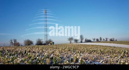 5G-Funkrelaisantenne auf einem schneebedeckten Feld im Kraichgau. Die Strahlung wird durch transparente Objekte symbolisiert. Stockfoto