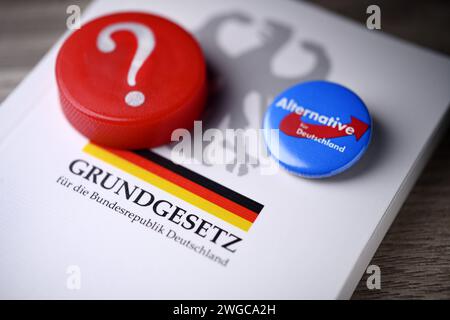 Parteianstecker der AfD und Fragezeichen auf dem deutschen Grundgesetz, Symbolfoto für die AfD-Verbotsdebatte *** AfD-Parteiabzeichen und Fragezeichen zur deutschen Verfassung, symbolisches Foto für die AfD-Verbotsdebatte Stockfoto