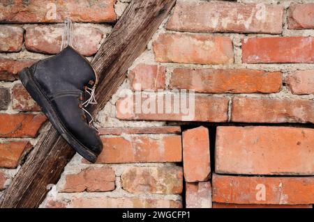 Ein alter schwarzer Schuh, der an einem Nagel an einer Ziegelwand hängt Stockfoto