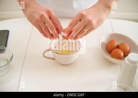 Nahaufnahme von weiblichen Händen, die Ei in eine Schüssel auf dem Küchentisch knacken. Prozess des Kochens von Pekannkuchen in der Küche für den amerikanischen Thanksgiving Day. Stockfoto