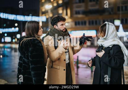 Drei junge Erwachsene diskutieren nachts auf einer Straße der Stadt mit hellen Lichtern und festlicher Atmosphäre. Stockfoto