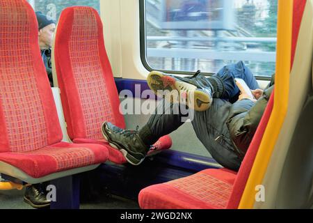 Nahaufnahme eines männlichen Fahrgastes in einem Vorortzug mit dem Fuß auf einem leeren Sitz Stockfoto