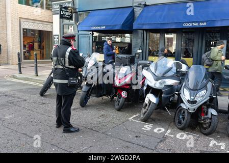 Ein Parkwächter, der einen Strafzettel für Motorräder ausstellt, die außerhalb eines ausgewiesenen Bereichs in der Stadt London, England, Großbritannien, geparkt sind Stockfoto