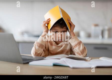 Probleme Beim Homeschooling. Gestresster Schwarzer Junge, Der Während Der Hausaufgaben Den Kopf Mit Dem Arbeitsbuch Bedeckt Stockfoto