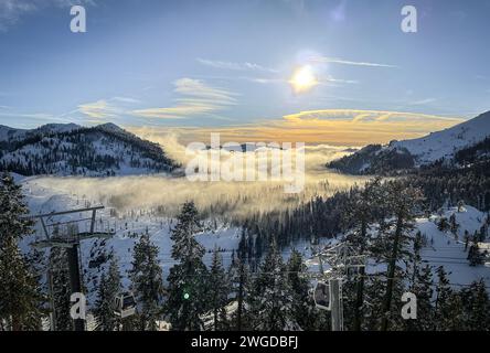 Einige Wolken ziehen sich tief durch Bäume auf einem schneebedeckten Berg in Lake Tahoe, Kalifornien bei Sonnenuntergang Stockfoto