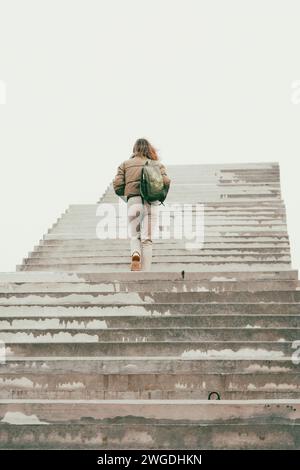 Frau, die auf der Treppe ins Nirgendwo läuft. Mädchen klettert die Treppe hoch. Person auf unvollendeter Brücke. Treppe zum Himmel. Treppen zum Erfolg. Karriereleiter. Stockfoto