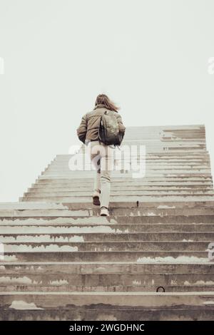 Frau, die auf der Treppe ins Nirgendwo läuft. Mädchen klettert die Treppe hoch. Person auf unvollendeter Brücke. Treppe zum Himmel. Treppen zum Erfolg. Karriereleiter. Stockfoto