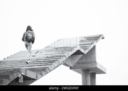 Frau, die auf der Treppe ins Nirgendwo läuft. Mädchen klettert die Treppe hoch. Person auf unvollendeter Brücke. Treppe zum Himmel. Treppen zum Erfolg. Karriereleiter. Stockfoto