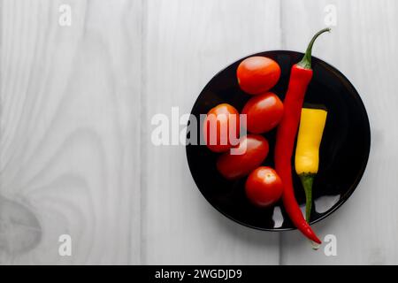 Anderthalb heiße Paprika auf einem schwarzen runden Teller. Kirschtomaten. Heller Hintergrund. Whiteboards. Gewürze in der Küche. Stockfoto
