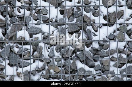 Verschneite Gabion, Textur, Hintergrund. Fragment des Gabionennetzes (Design), mit Schnee gefüllt. Neue Technologien bei der Herstellung von Stützmauern und Zäunen Stockfoto