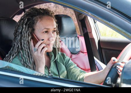 Geschäftsfrau im Auto, die aufmerksam jemandem am Telefon zuhört. Porträt einer attraktiven asiatischen Frau Stockfoto
