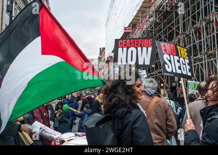 London, Großbritannien. Februar 2024. Waffenstillstand jetzt und Ende der Belagerungsbanner, die von Friedensaktivisten und Demonstranten während des Pro-Palästina-protestmarsches durch die Oxford Street in Soho, Bewegung der Freien Palästinenser, gehalten wurden. Eine Frau hält eine palästinensische Flagge. London, Großbritannien Stockfoto