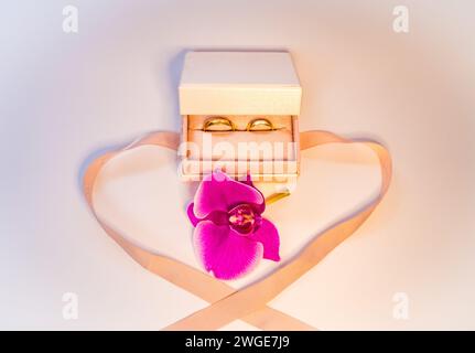 Eheringe in Geschenkbox mit violetter Orchidee. Goldschmuck. Hochzeit Stockfoto