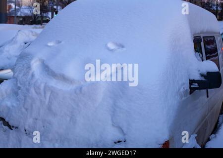 Der geparkte Minibus ist komplett mit tiefem Schnee bedeckt und hat ein lächelndes Gesicht darauf. Stockfoto