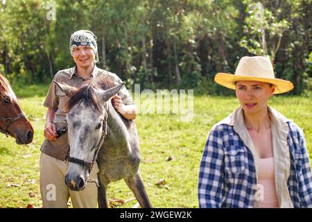 Lächelnd, junger Mann neben braunem Pferdefohlen, verschwommene Frau in der Nähe, Dschungelbäume Hintergrund - reiten in Isalo, Madagaskar Stockfoto