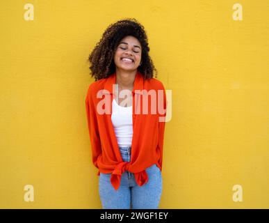 Sorglos lächelnde afroamerikanische junge Frau, die mit einer gelben Wand im Hintergrund lächelt Stockfoto