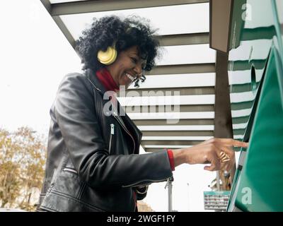 Afroamerikanerin mittleren Alters in einer Stadt, die in einer Stadt ein Ticket für öffentliche Verkehrsmittel kauft. Konzept des öffentlichen Nahverkehrs Stockfoto