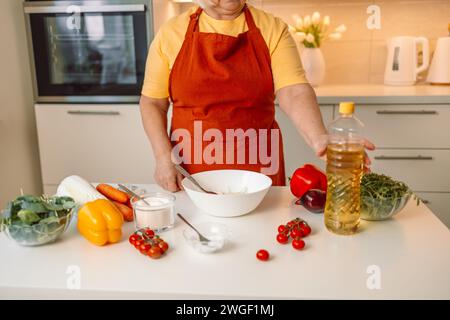 Weibliche Chefin in einer Uniform gießt Olivenöl aus einer Flasche. Kaukasische Bloggerin, die erklärt, wie man ein Gericht kocht Stockfoto