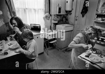 Arbeiterfamilie 1970s UK, zu Hause Fulham London 1972. Das ist ihre Küche. Sie hatten kein eigenes Bad, das man mit anderen Familien im Haus teilen konnte. Das Butler-Waschbecken wird morgens zum Waschen des Gesichts verwendet. Der Küchentisch ist nicht groß genug, um herumsitzen zu können. Mutter benutzt den kleinen Tisch, wenn sie alle zusammen essen. Baby im Hochstuhl. HOMER SYKES Stockfoto