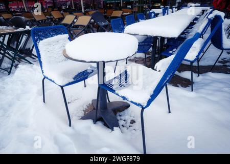 Viel Schnee auf Tischen und blauen Stühlen in der touristischen Outdoor-Gastronomie in der kölner Altstadt Winter 2024 Stockfoto